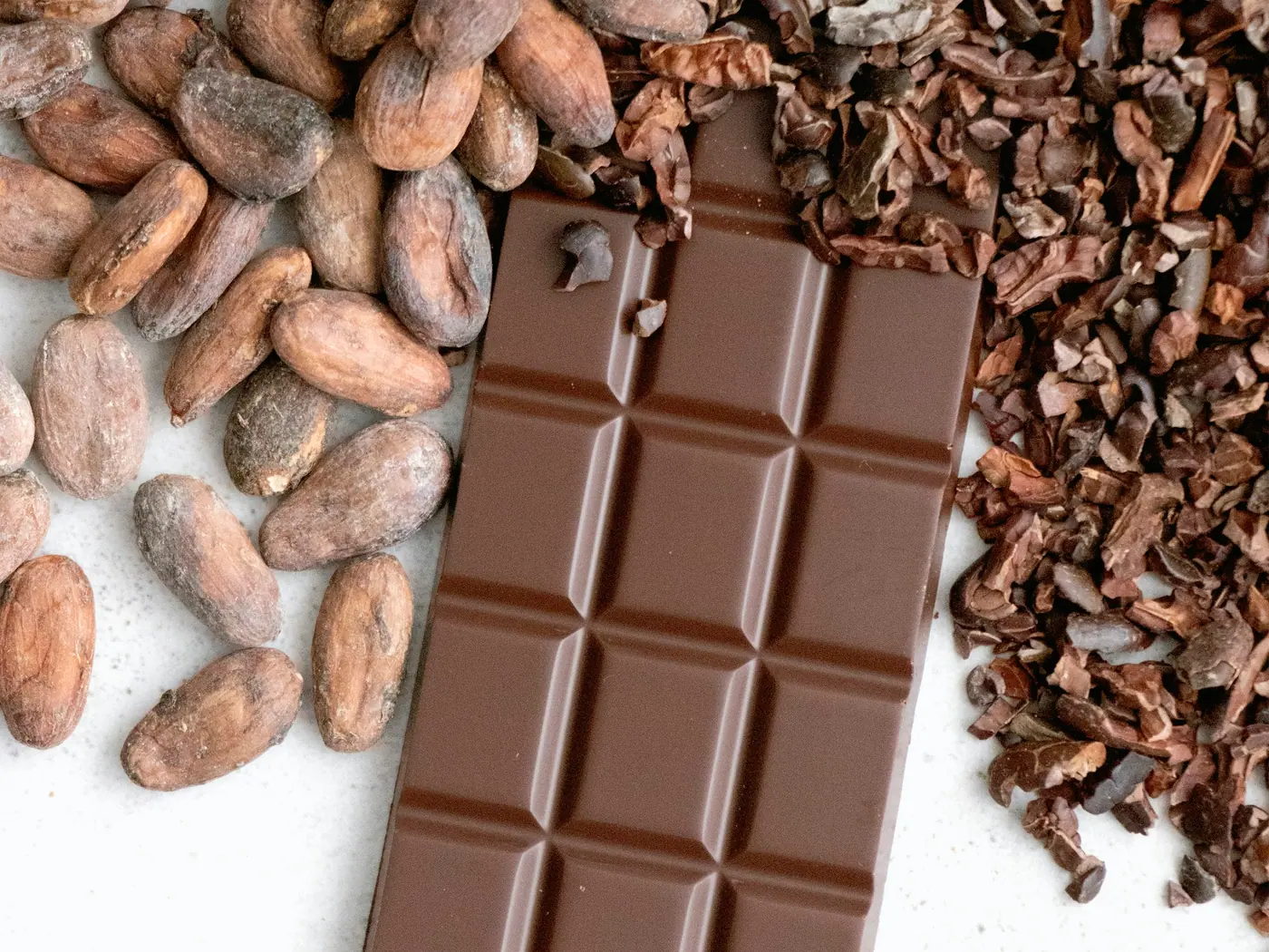 Chocolate, amêndoas de cacau e nibs dispostos sobre uma superfície escura
