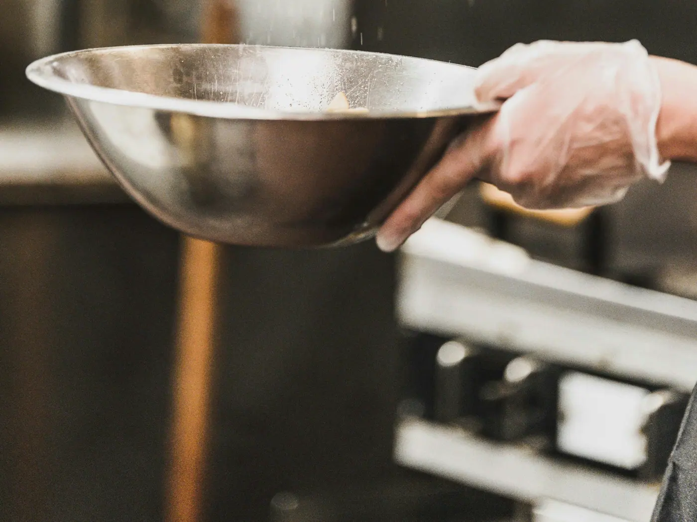 Profissional finalizando uma preparação em uma tigela de inox